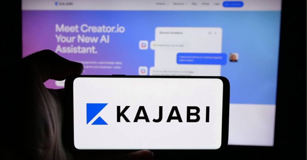 Logo de Kajabi en un smartphone con la interfaz de la plataforma en el fondo.