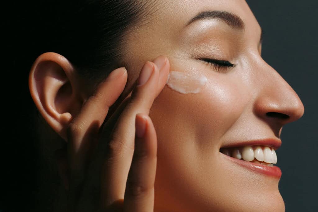mujer joven aplicandose crema en la cara refiriendose a Cuidado de la Piel